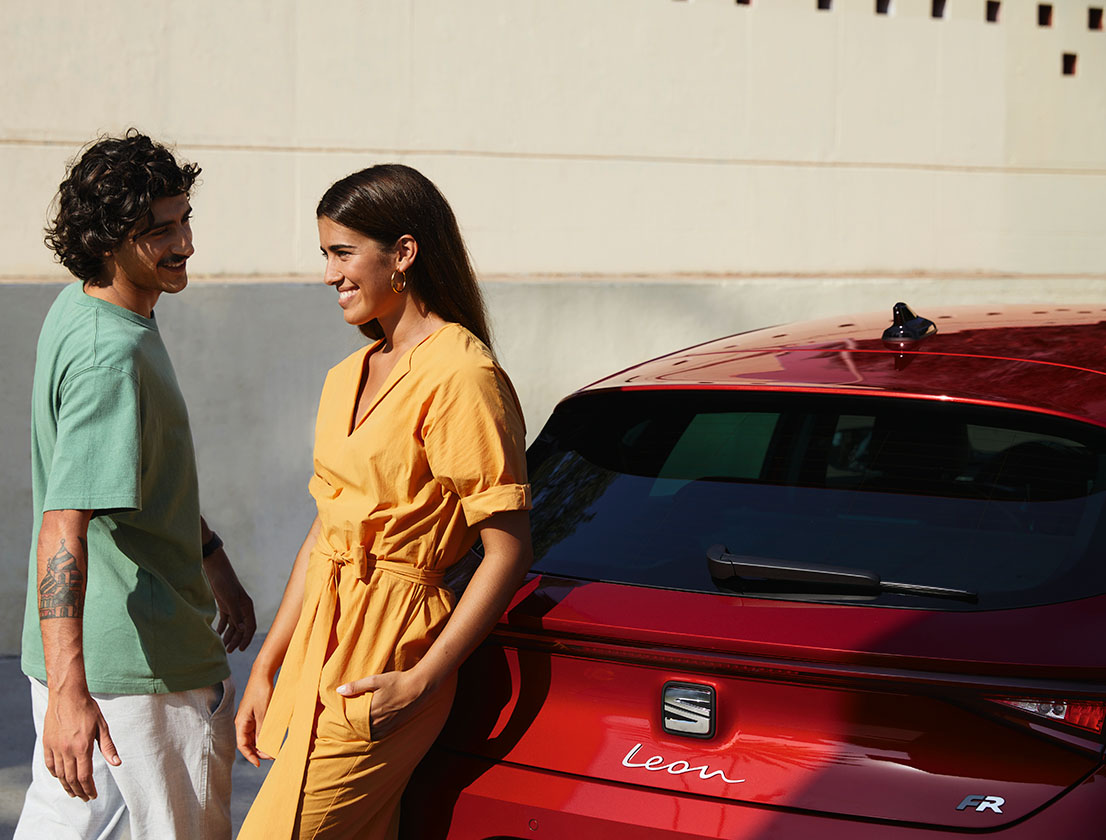 pareja hablando junto a un SEAT León color rojo Desire