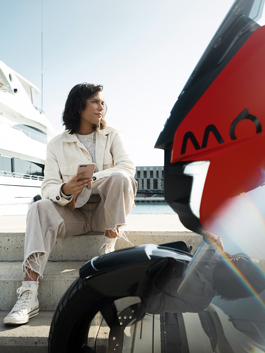 Mujer sentada junto a su scooter SEAT MÓ 125 eléctrico estacionada en el puerto